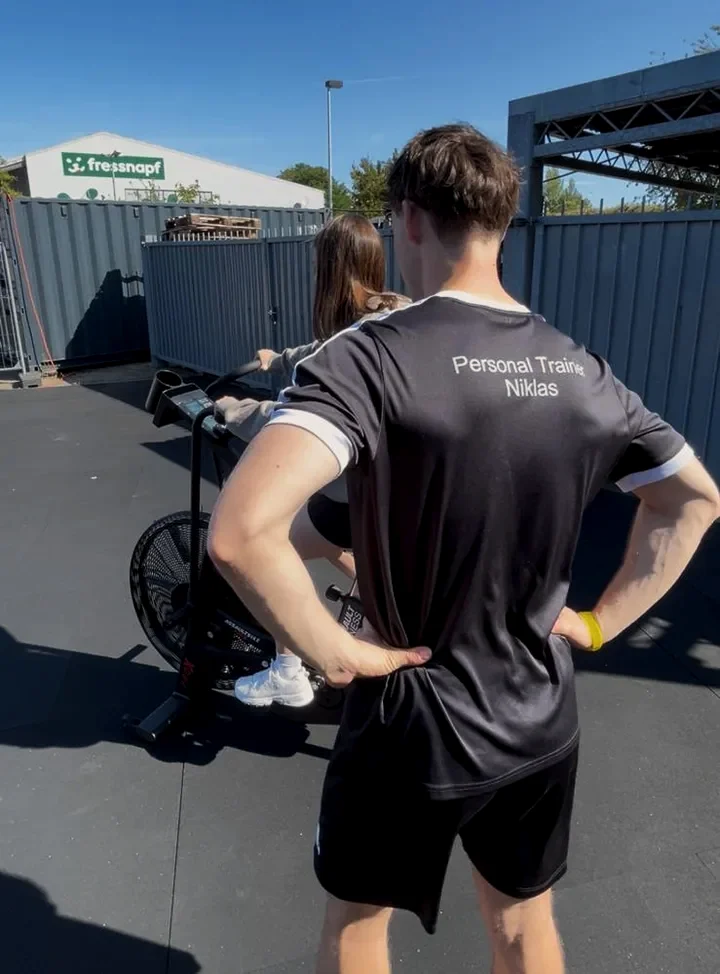 Niklas Donner betreut eine Kundin auf dem Assault Bike im Hyrox-Bereich